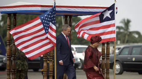 AFP/Getty Images Former US President George W Bush and former Liberian President Ellen Johnson Sirleaf walk past Liberian and US flags in February 2008.